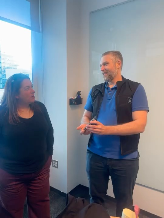 Brad wearing the Tactus vest, showing Julie his phone, which is playing the music for the vest